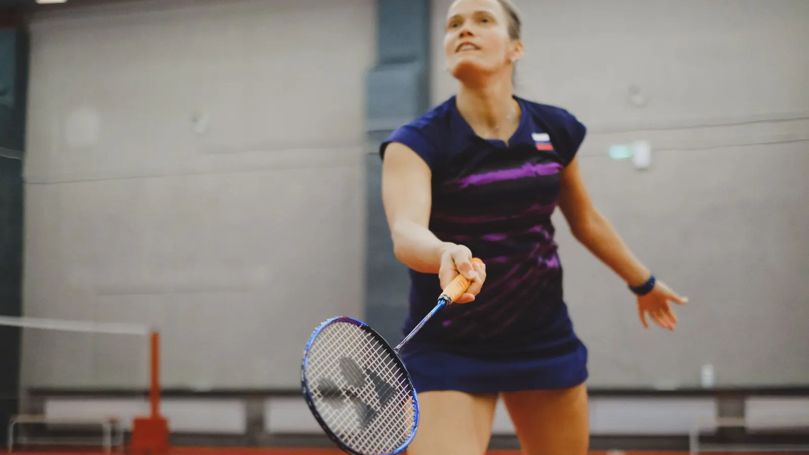 A badminton player mid stroke on an indoor court