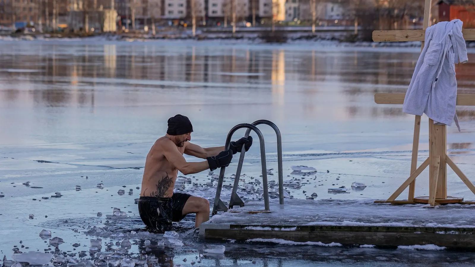 A man lowering himself into a hole cut in a frozen lake