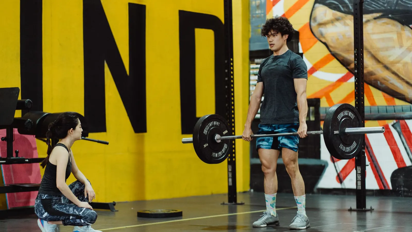 A man setting up a deadlift while a trainer watches his form