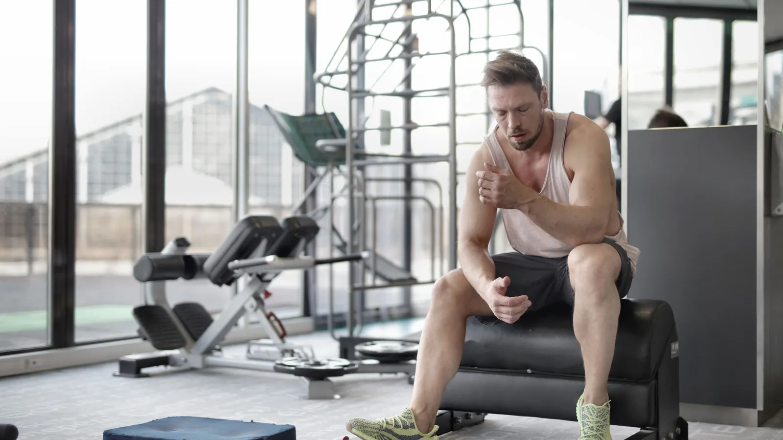 A man resting on a gym bench looking fatigued after training