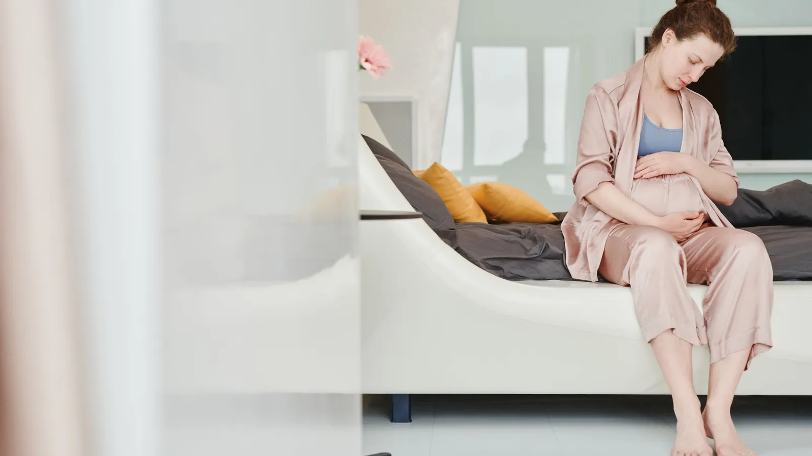 A pregnant woman sitting on a bed resting a hand near her hip