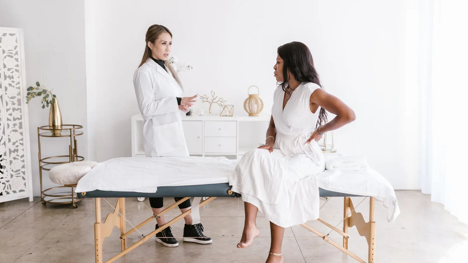 A patient with a hand on her lower back talking to a practitioner