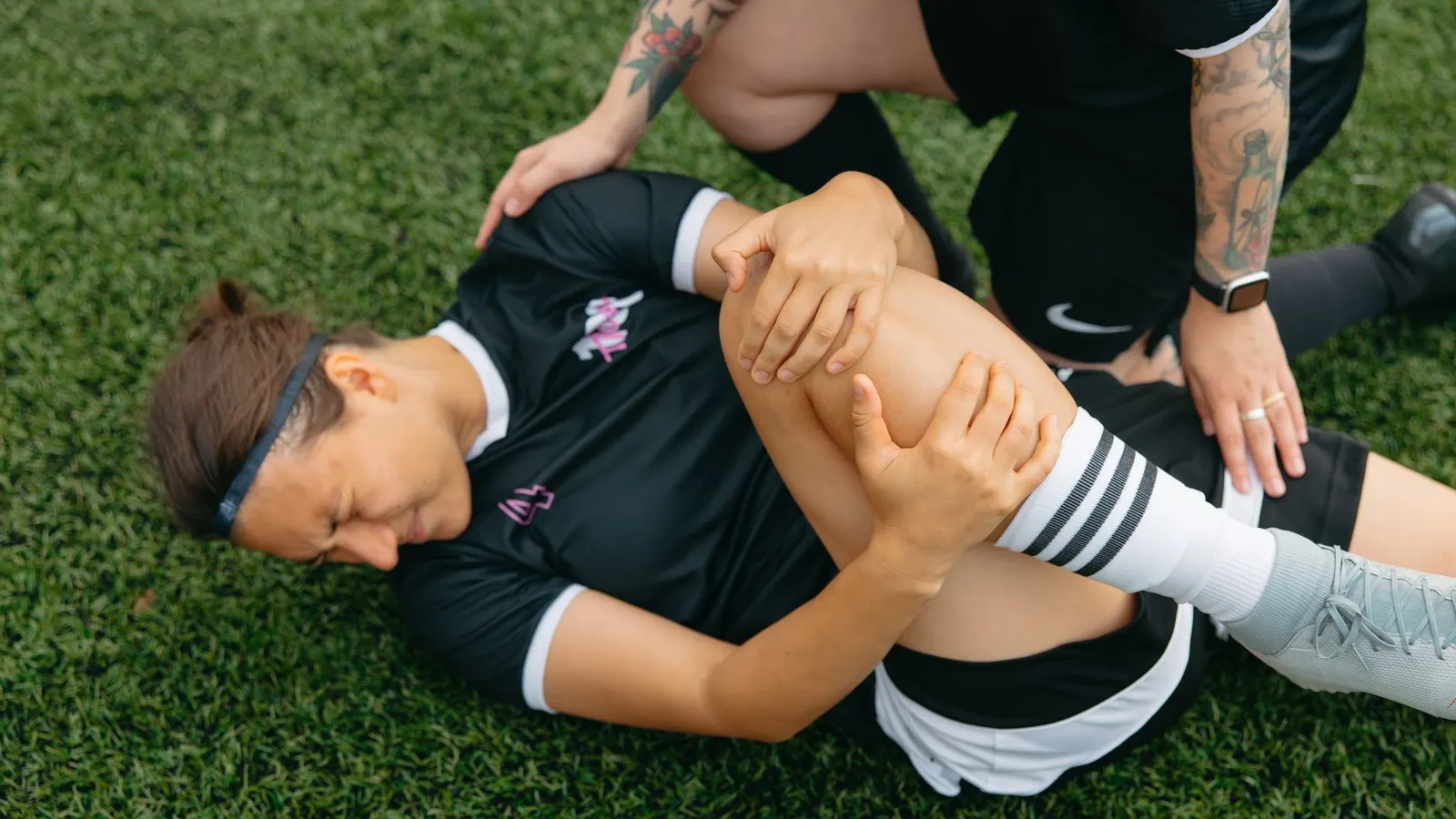 An injured athlete on the field holding her knee while a physio attends