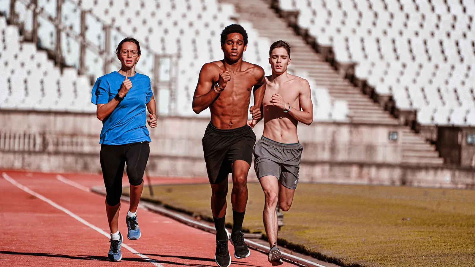Three runners training together on an athletics track