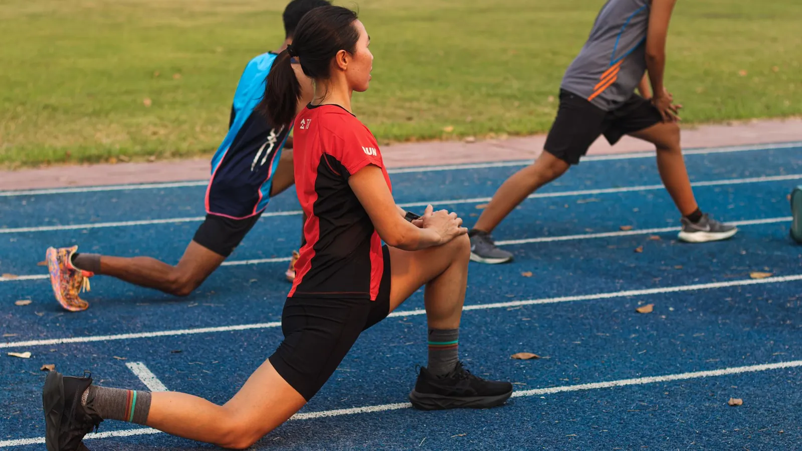 Two athletes doing lunge warm up drills on a track