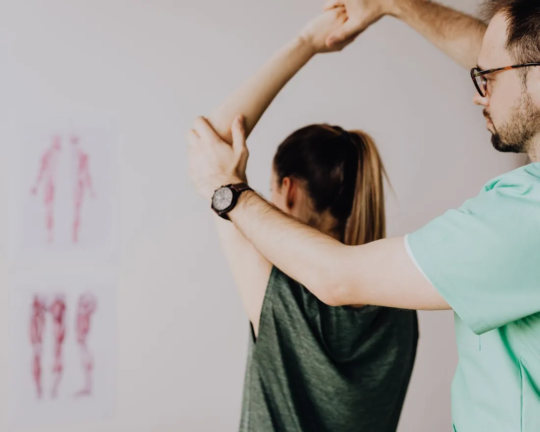A physiotherapist guiding a patient's raised arm through an overhead shoulder stretch